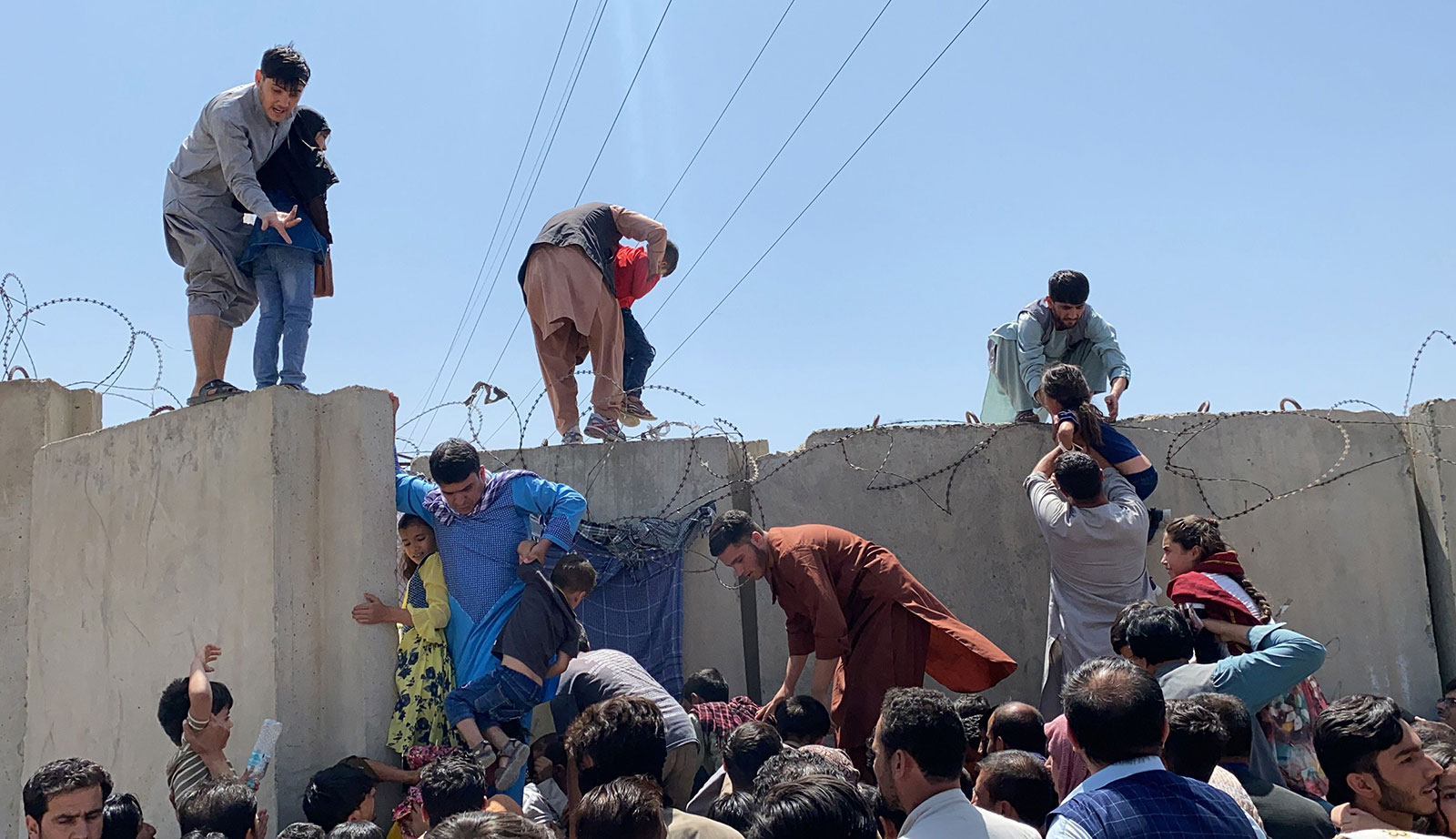 People struggle to cross the boundary wall of Kabul's Hamid Karzai international airport on August 16.