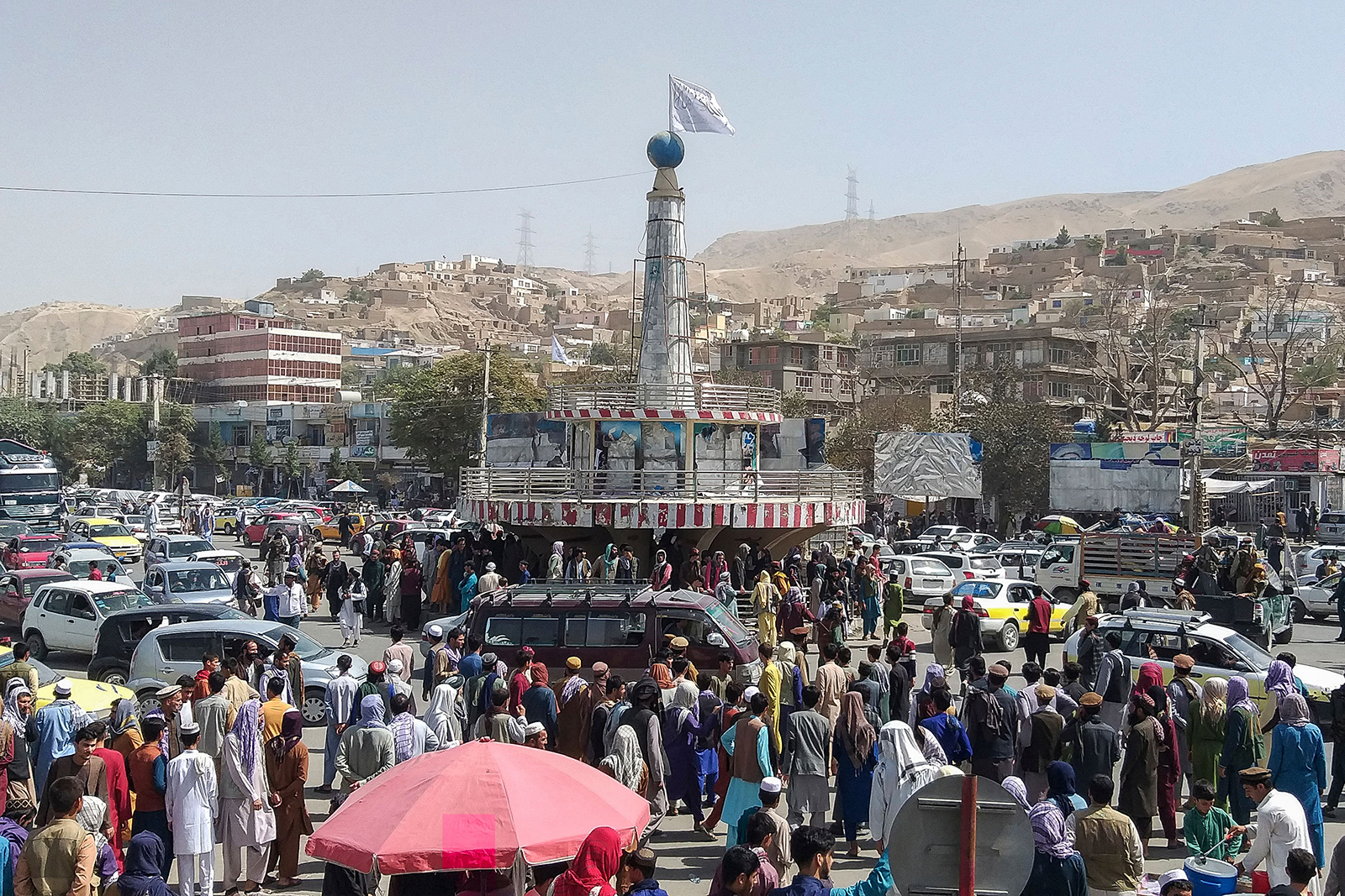 A Taliban flag is seen on a plinth with people gathered around the main city square at Pul-e-Khumri on August 11.